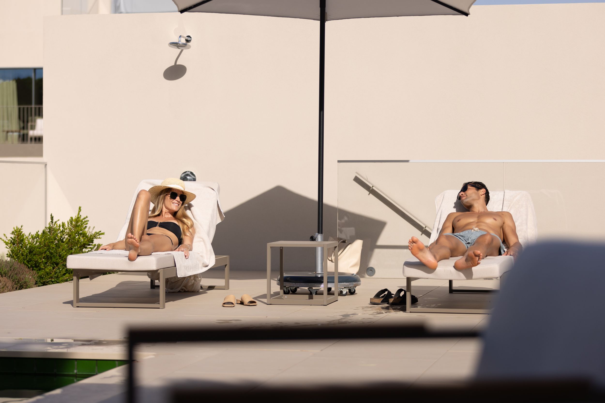 Two lounge chairs on a sunny terrace with umbrella beside modern swimming pool.
