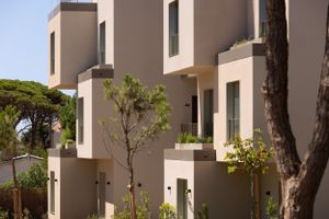 Contemporary beige apartment buildings with geometric architecture and balconies among trees.