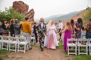 Wedding celebration with guests walking down aisle near red rock formations in natural outdoor setting.