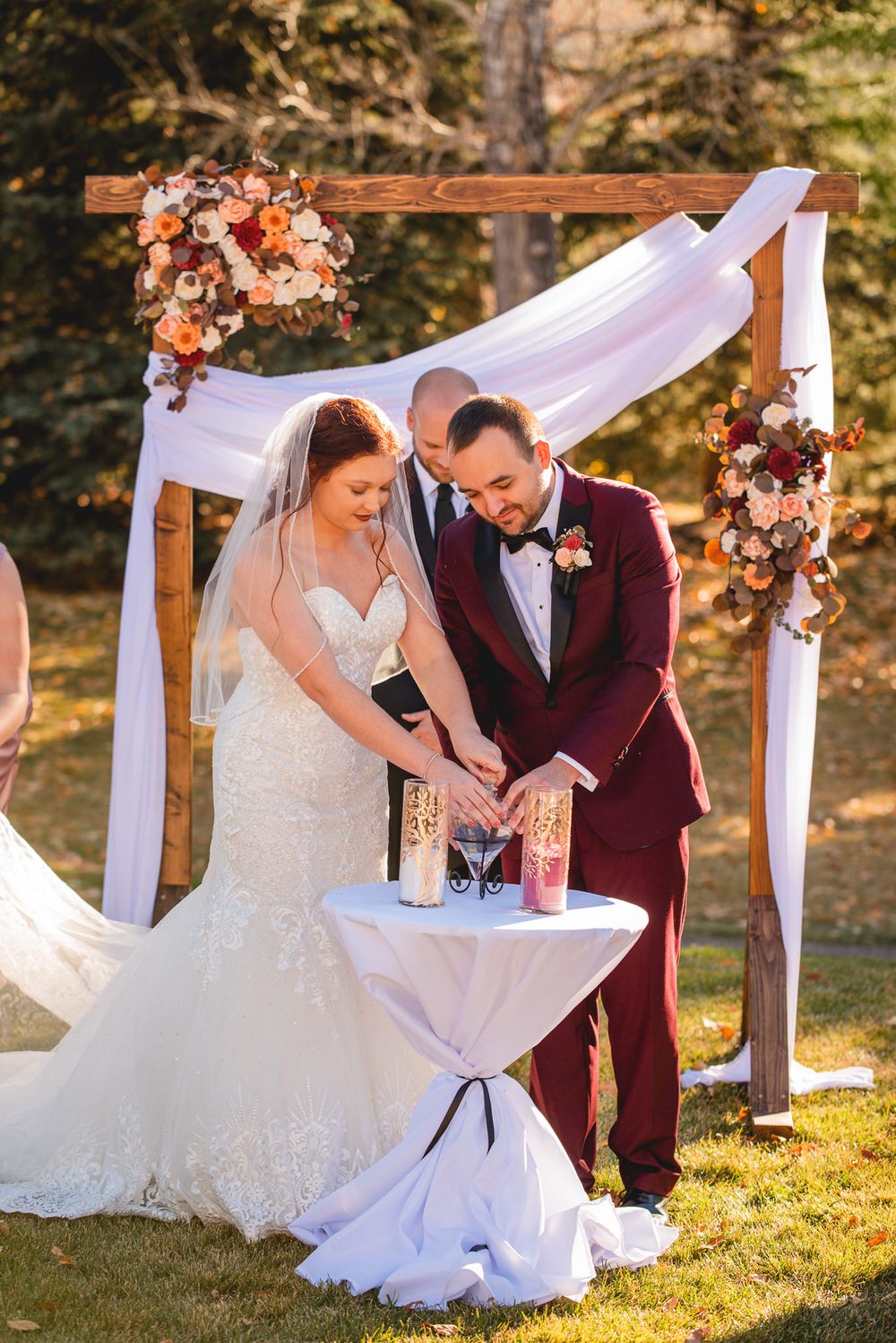 Couple performing unity sand ceremony under wooden arch with floral decorations.