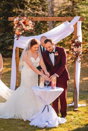 Couple performing unity sand ceremony under wooden arch with floral decorations.