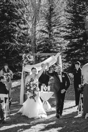 Black and white photo of newlyweds joyfully exiting their outdoor ceremony.