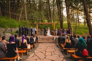 Outdoor forest wedding ceremony with wooden benches and string lights at dusk.