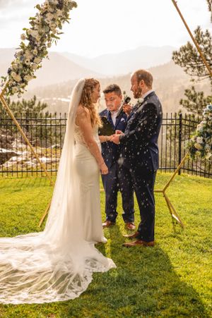 Outdoor mountain wedding ceremony with snow falling during vows under a floral arch.