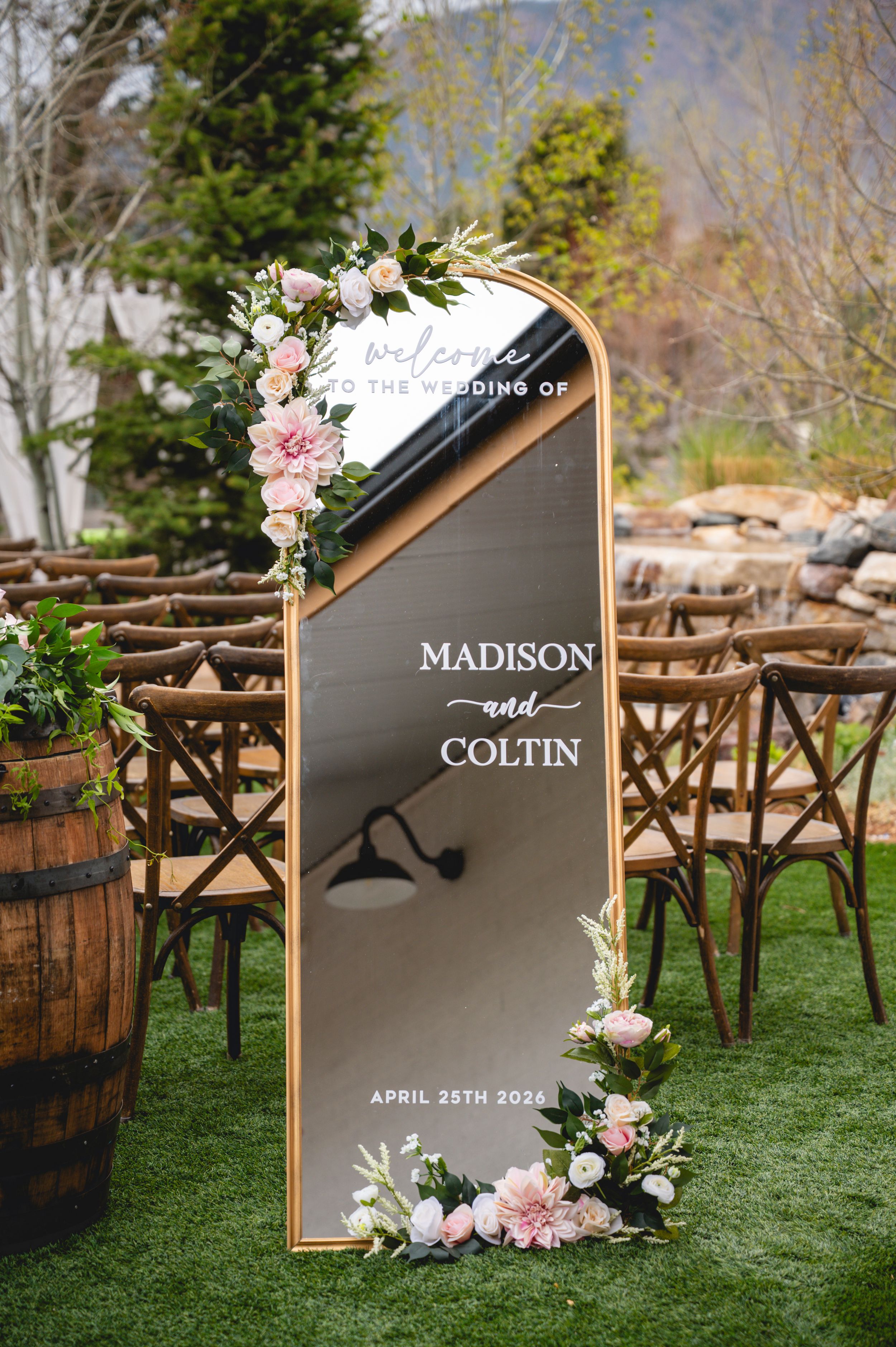 Elegant wedding welcome mirror sign for Madison and Coltin, April 25th 2026, adorned with pink florals outdoors.