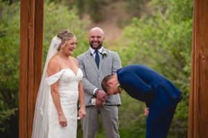 Wedding ceremony taking place under a wooden arch in a natural outdoor setting.