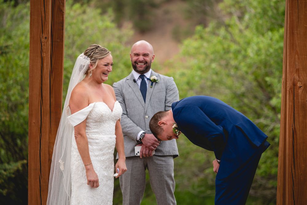 Wedding ceremony taking place under a wooden arch in a natural outdoor setting.