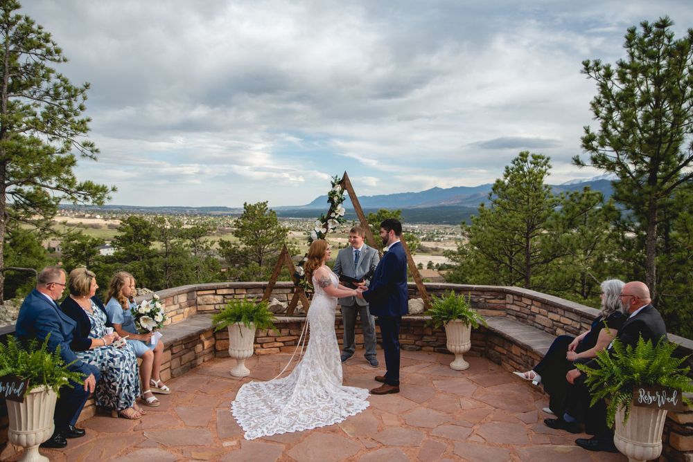 Wedding ceremony on curved stone patio overlooking mountain landscape with dramatic cloudy sky.