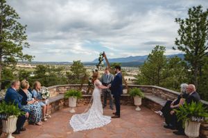 Wedding ceremony on curved stone patio overlooking mountain landscape with dramatic cloudy sky.