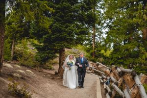 Couple walking down forest path surrounded by evergreen trees in mountain setting.