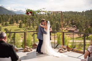 A wedding ceremony under a floral arch with mountain views and evergreen forests in the background.