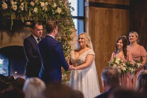 Indoor wedding ceremony under floral arch with rustic barn wood backdrop.
