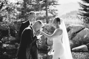 Black and white emotional moment during mountain wedding ceremony with evergreen trees in background.