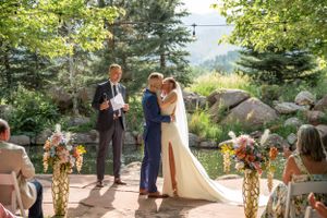 Outdoor summer wedding ceremony with floral decorations and mountain backdrop.