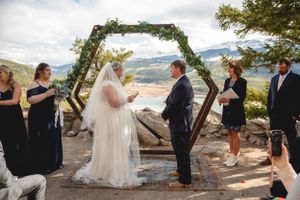 Mountaintop wedding ceremony under floral arch with scenic lake view.
