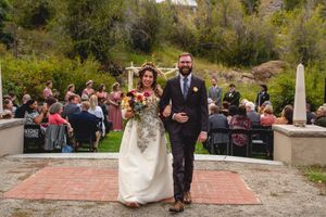 Wedding couple walking down brick aisle after outdoor ceremony with mountain backdrop and seated guests.