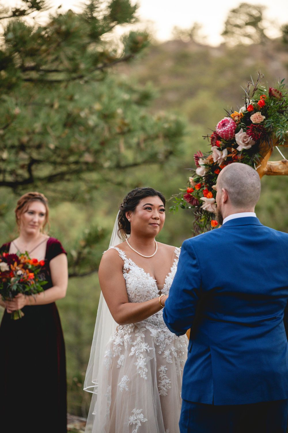 Outdoor wedding ceremony with burgundy and pink floral arch arrangements.