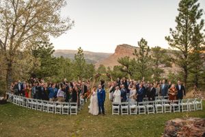 Panoramic view of outdoor wedding ceremony with white chairs and rocky mountain backdrop.