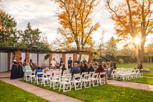 An outdoor fall wedding ceremony setup with white chairs and golden sunlight through trees.