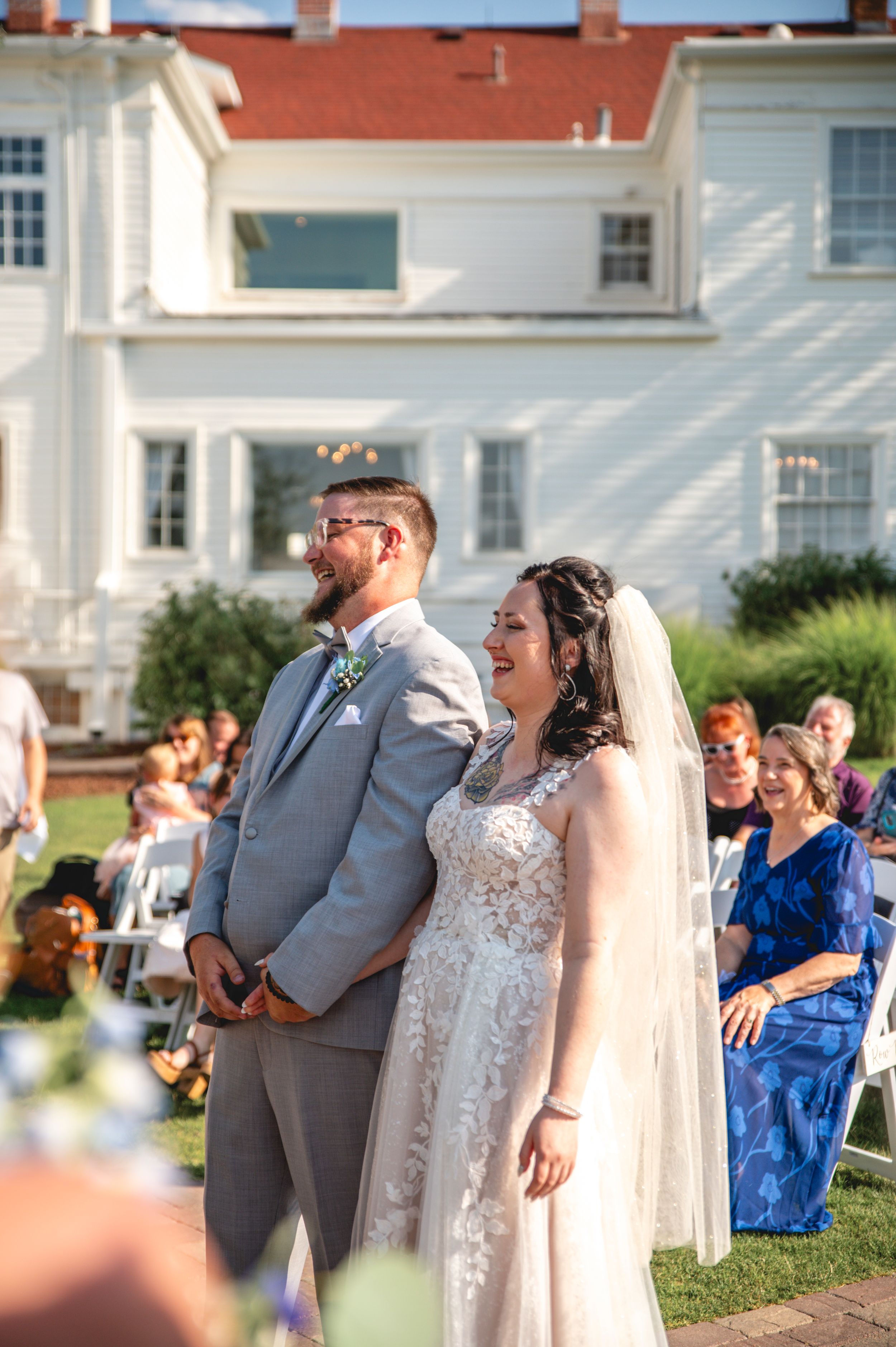 Outdoor wedding ceremony in front of historic white mansion with blue sky.