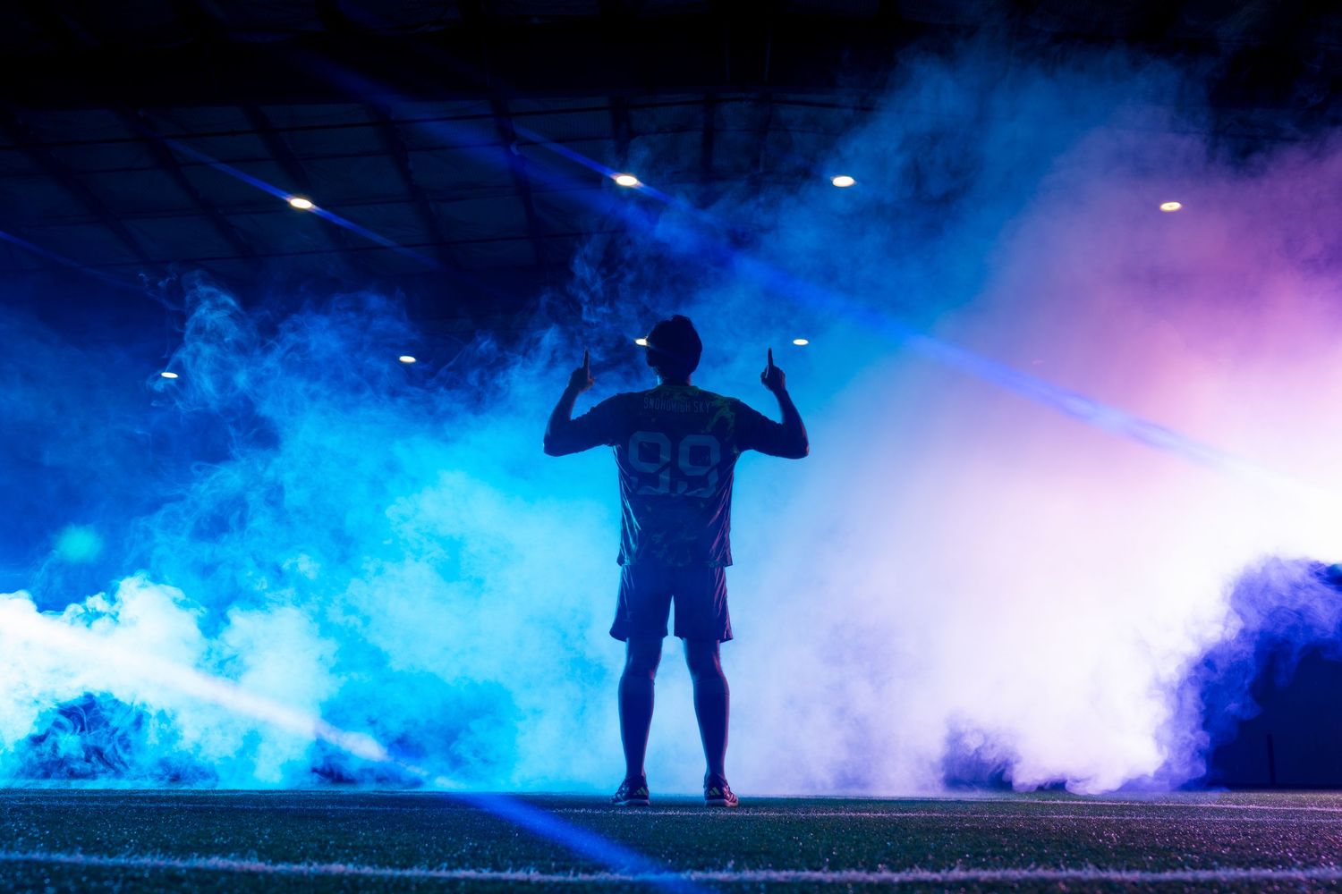 Silhouette of a performer standing on stage surrounded by dramatic blue and pink smoke effects with theatrical lighting.