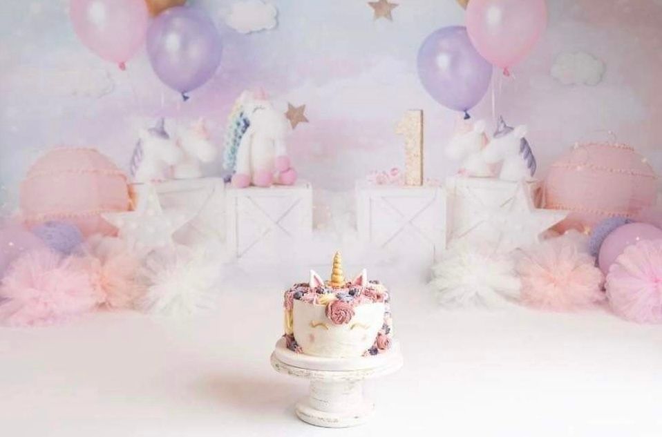 Pastel unicorn-themed birthday cake setup with balloons and dreamy pink backdrop for party photography.