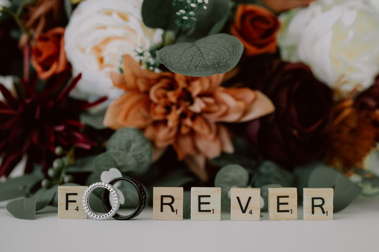 A rustic wedding decor display featuring wooden letter blocks spelling 'FOREVER' alongside autumn-colored floral arrangements.
