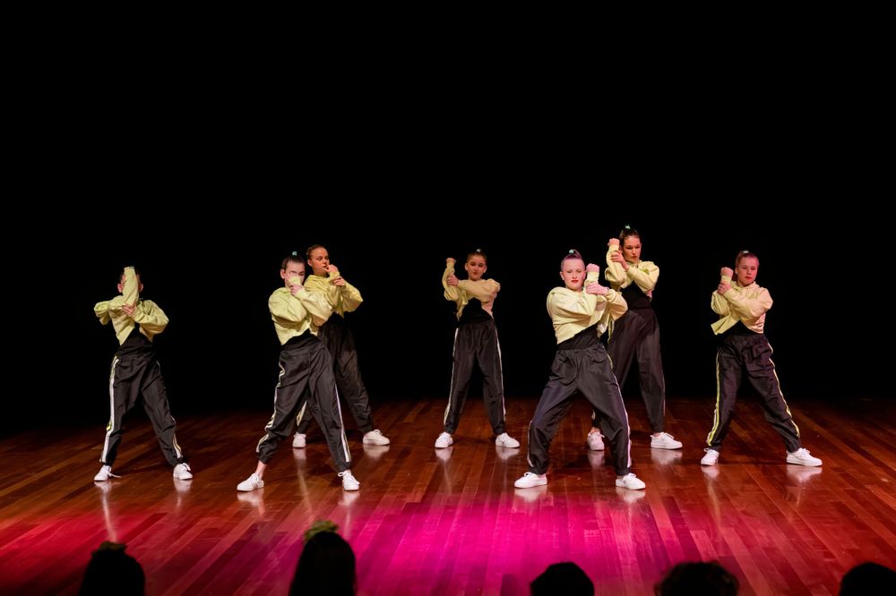 Dance group performs energetic routine in matching yellow and black outfits on wooden stage.