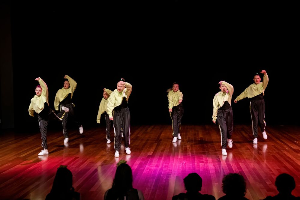 Dance ensemble performs synchronized moves in yellow and black costumes under stage lighting.