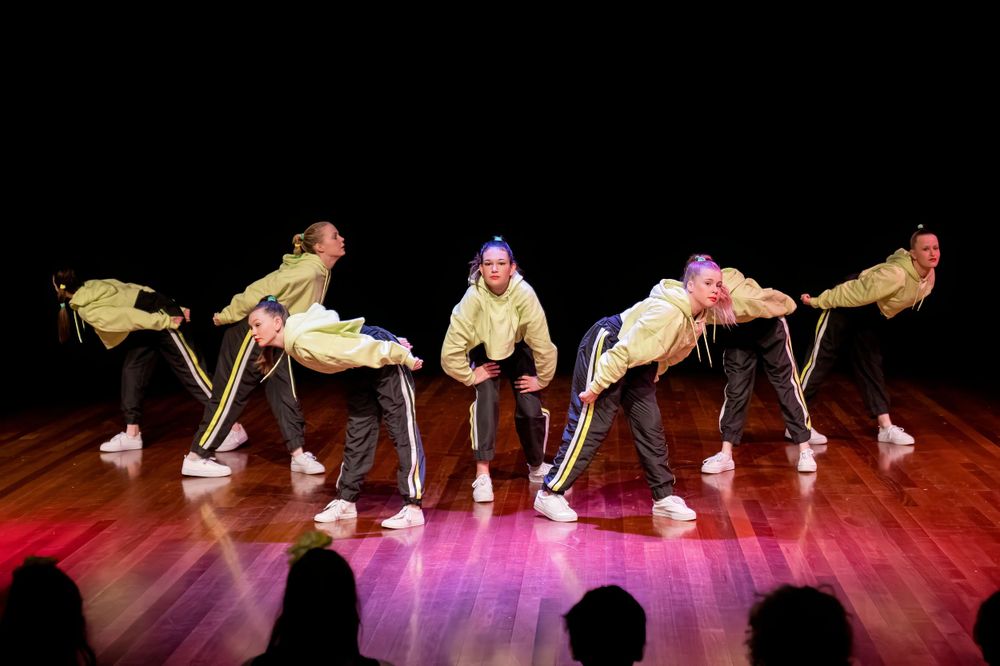 Dancers in yellow shirts create a leaning formation during stage performance.
