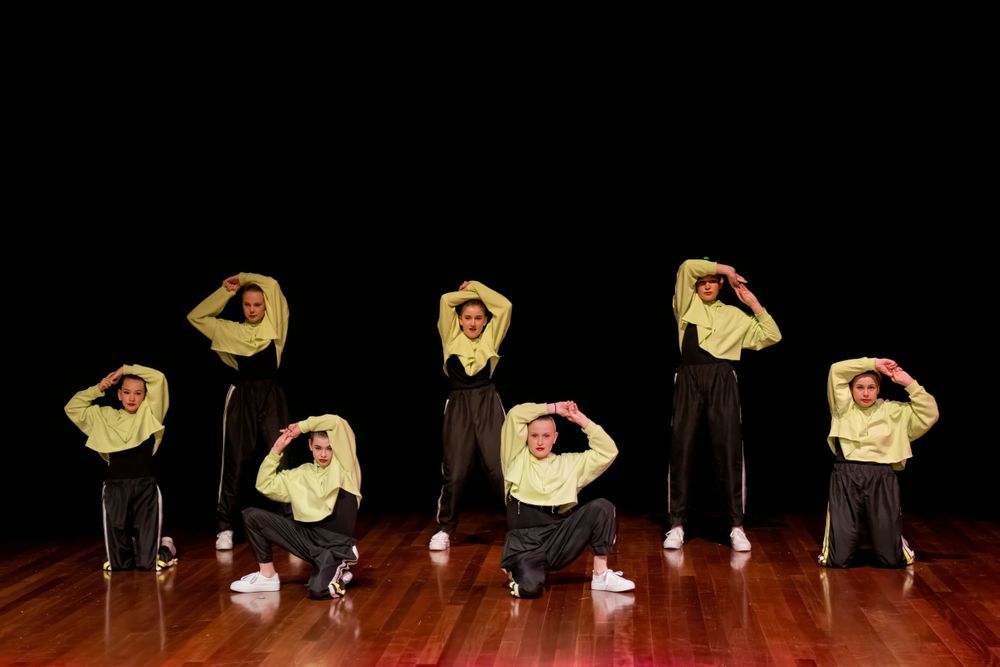 Dancers in yellow and black outfits perform a synchronized bending pose on stage.