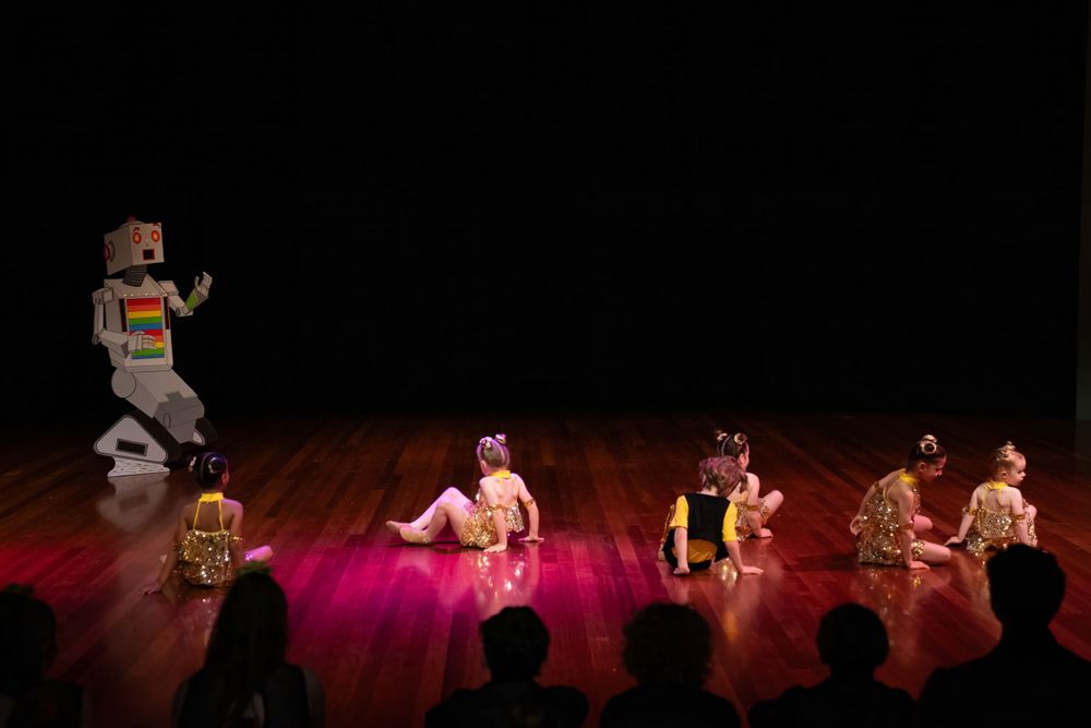 Theatrical dance scene with performers in tribal costumes under dramatic stage lighting.