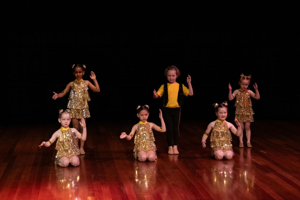 Young dancers perform a synchronized dance routine wearing coordinated outfits on a wooden stage.