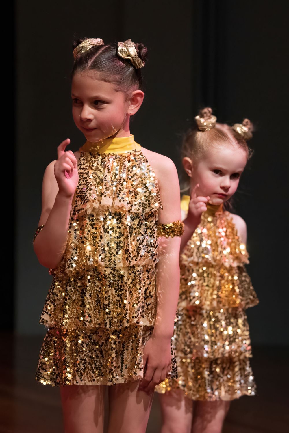 Two dancers in sparkly gold tiered dresses perform on stage.