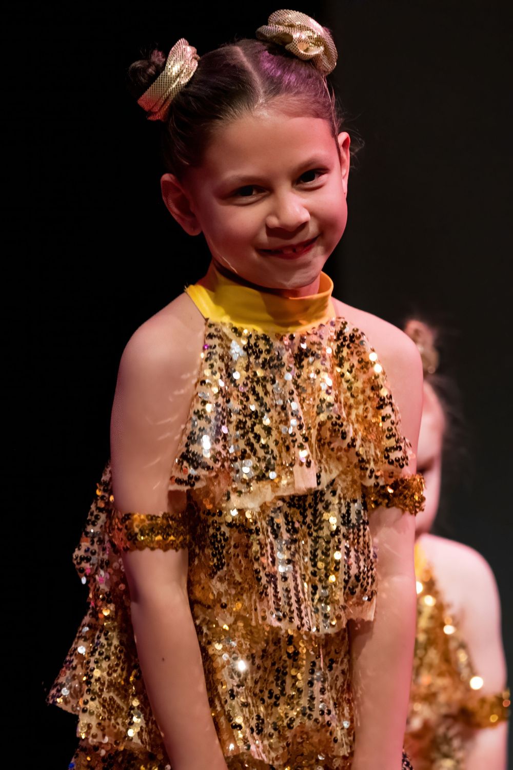 Performer in a shimmering gold sequined costume smiles during a dance recital.