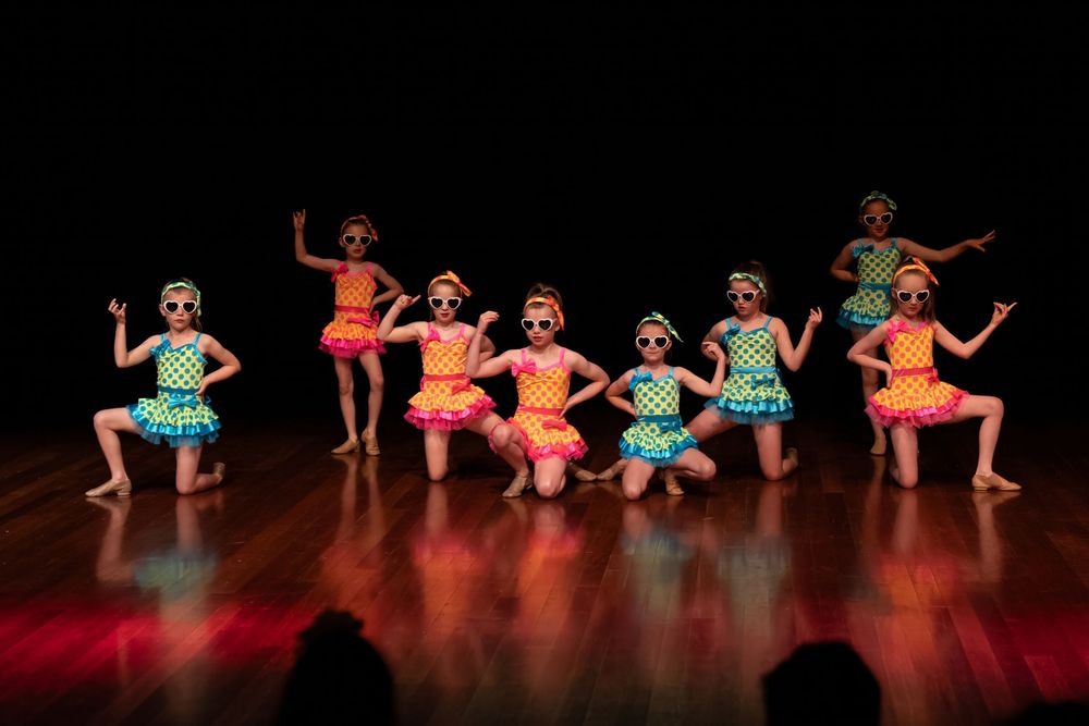 Dance group in bright turquoise and coral costumes strikes dynamic poses during performance.