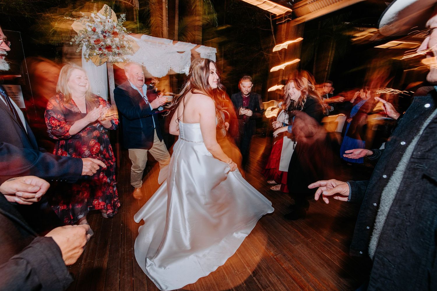 A bride in a flowing white dress twirls on the dance floor surrounded by guests.