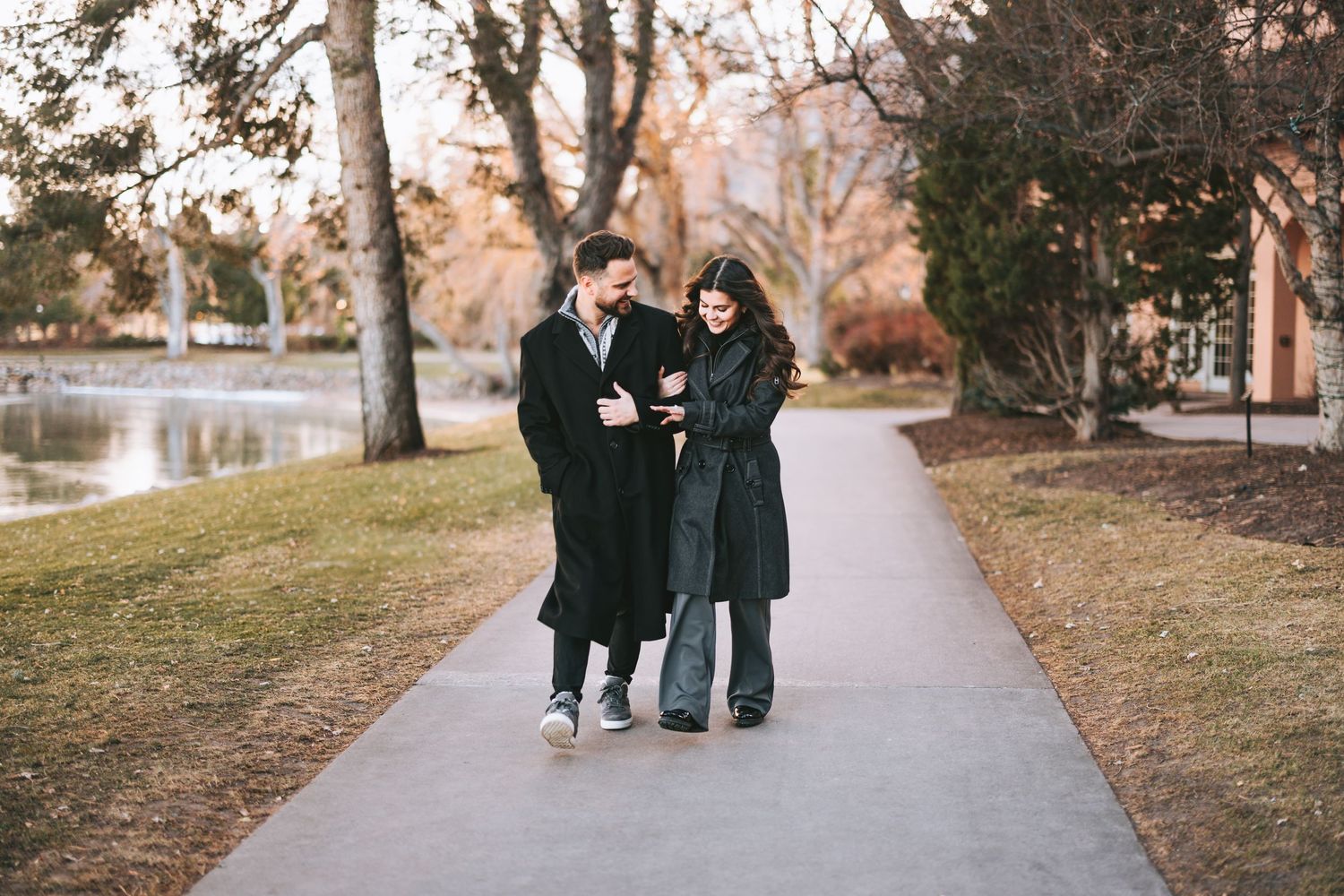 Three people in winter coats walking together on a paved path near bare trees.