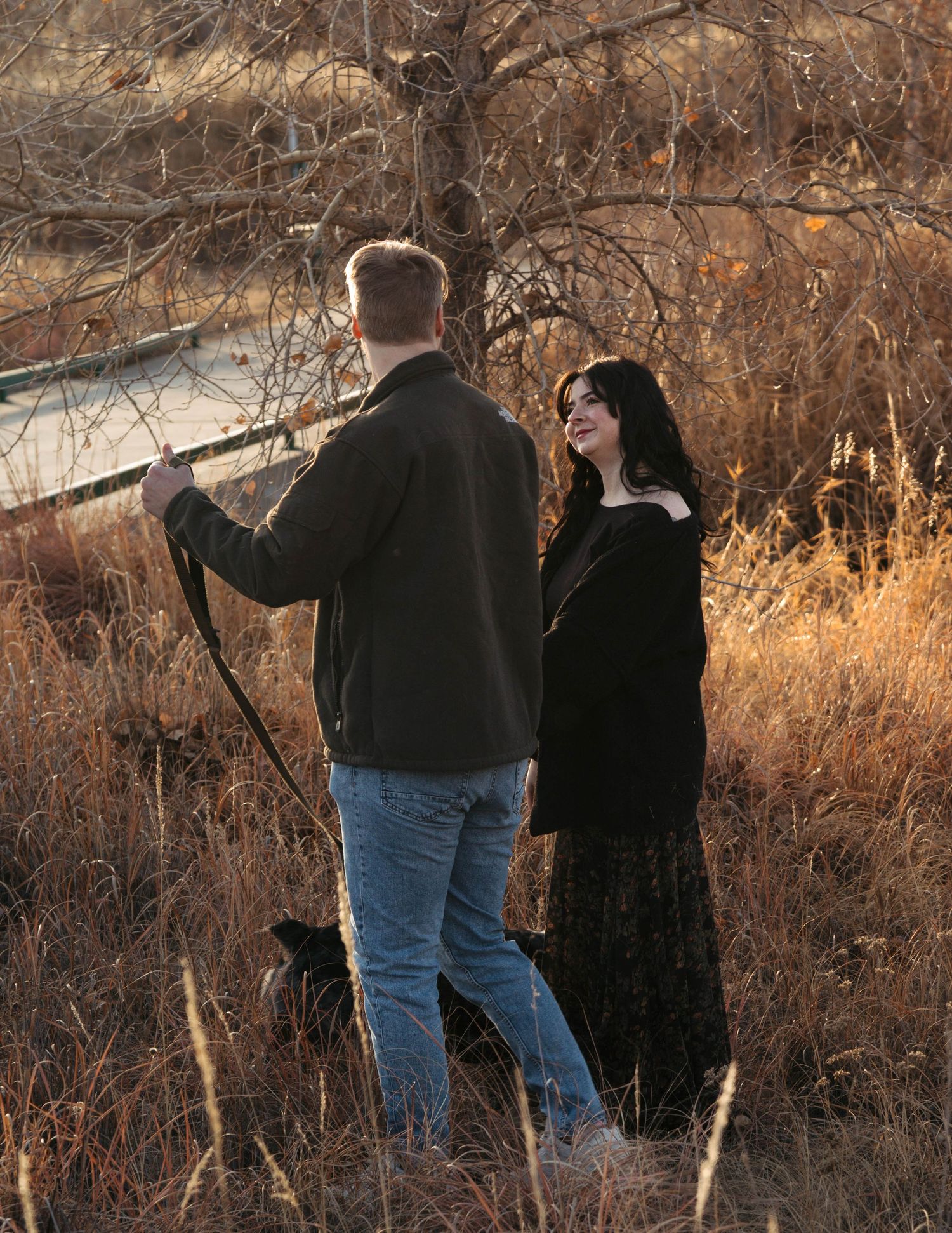 Two people stand together in autumn brush at sunset while looking off into the distance.