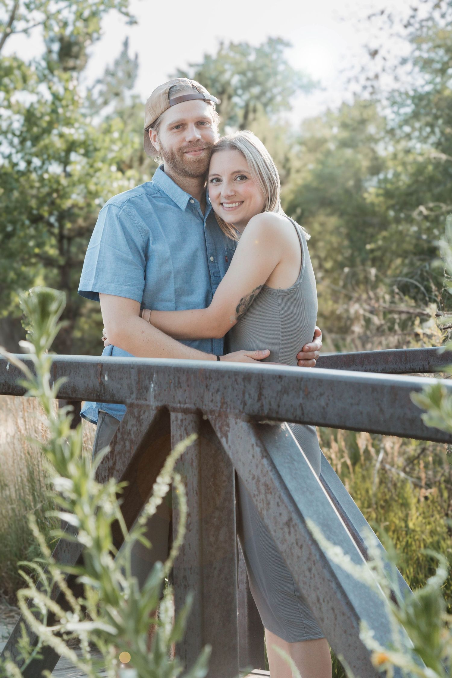 A couple shares an intimate moment while posing on a rustic bridge in nature.
