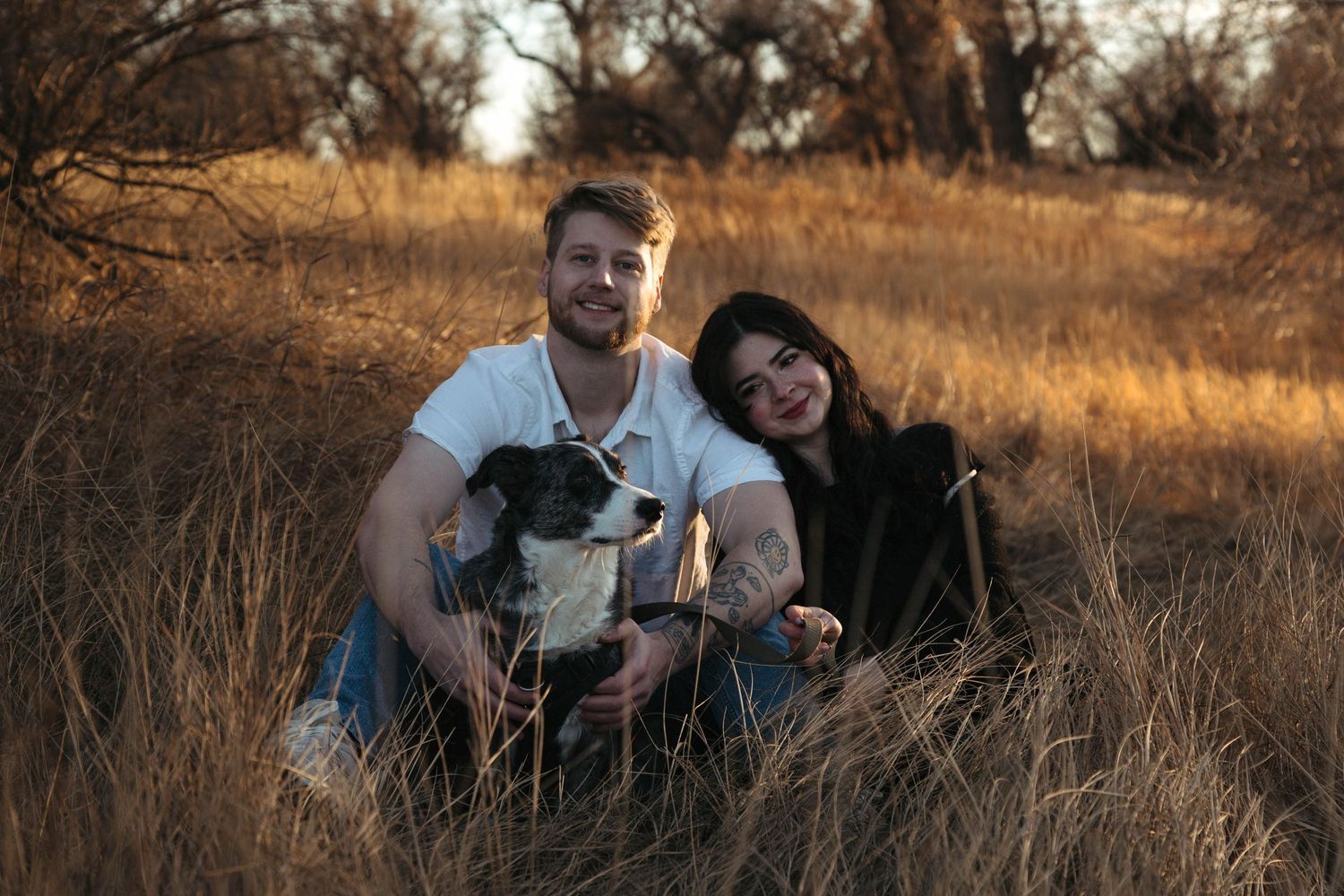 Couple sits together in golden autumn field during sunset photoshoot session.