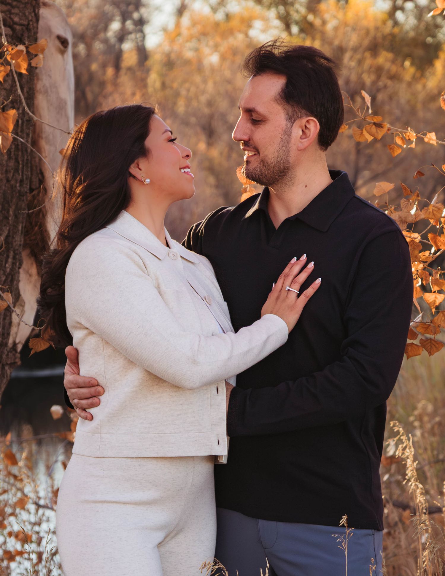 A couple embraces and laughs together in a romantic autumn setting with golden foliage in the background.