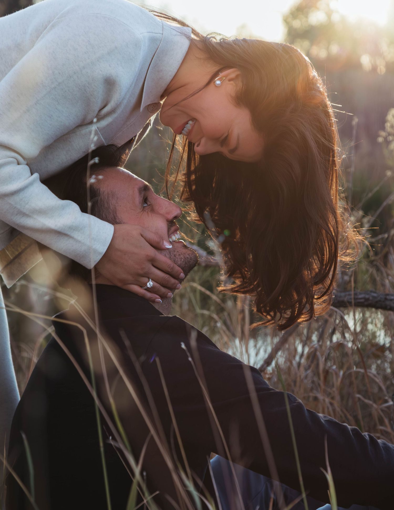 A couple shares an intimate moment in tall grass during golden hour sunset lighting.