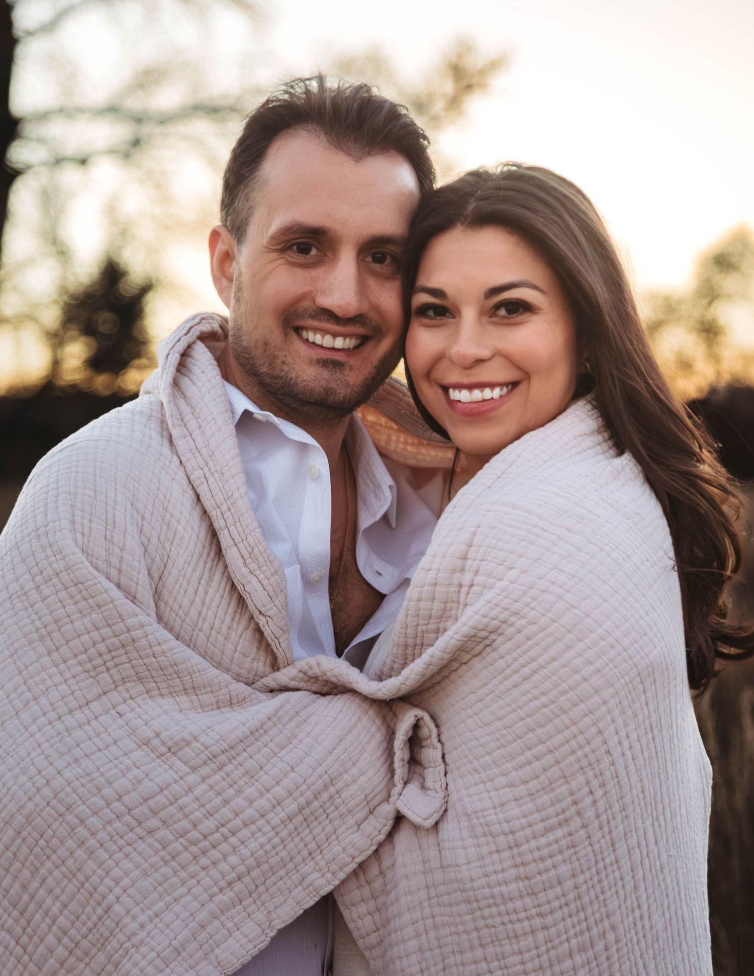 Romantic couple wrapped in a cozy beige blanket sharing intimate moments together outdoors at sunset.