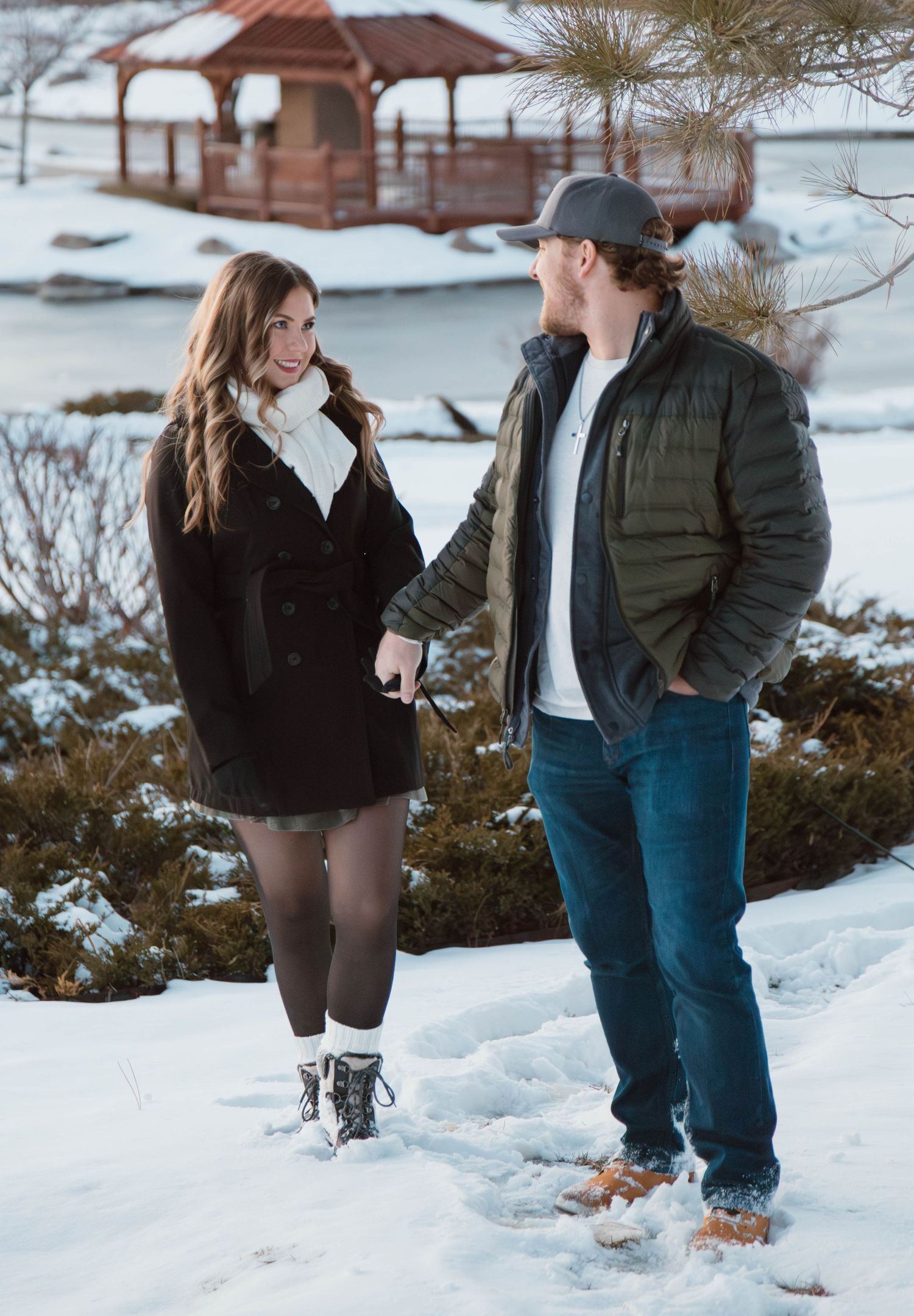 Couple standing in snowy landscape with gazebo in background.