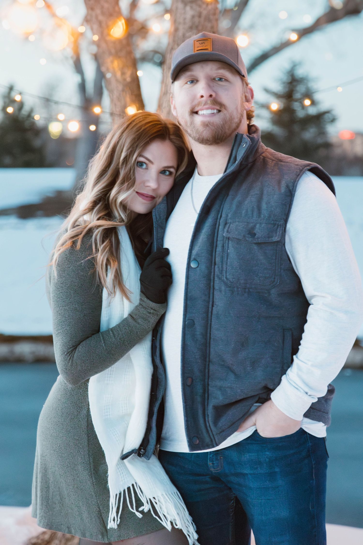 A cozy winter portrait of a couple against a snowy background with string lights.