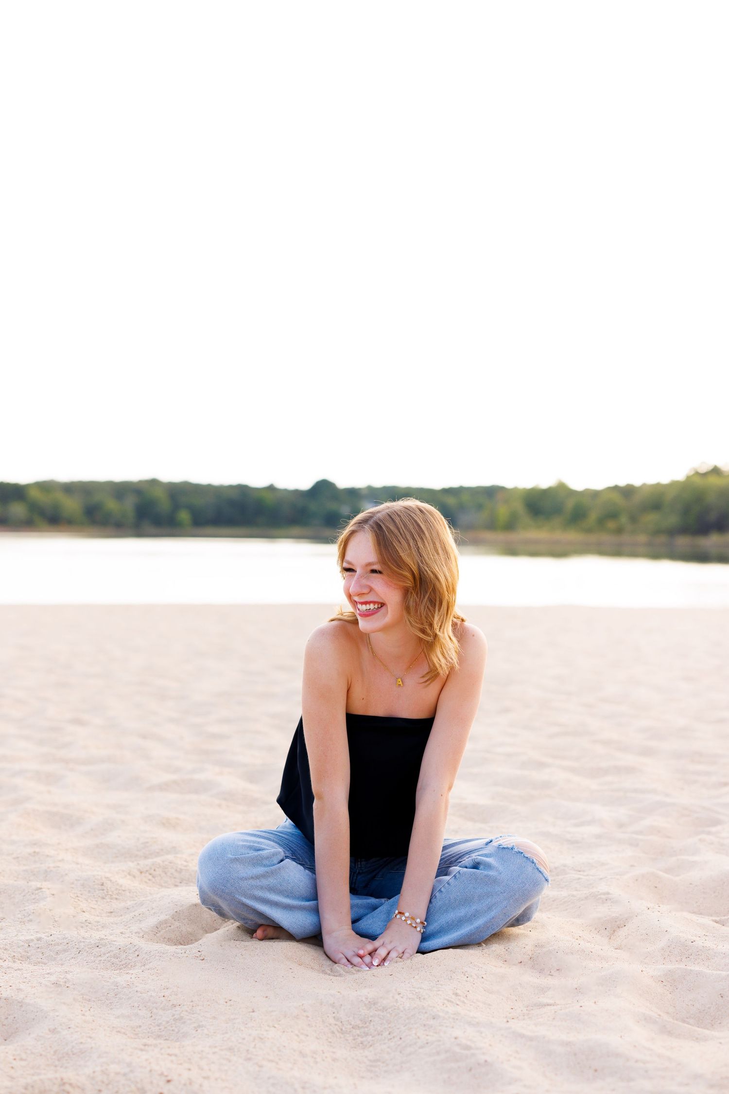 Person in black top and jeans relaxing on sandy beach at sunset.