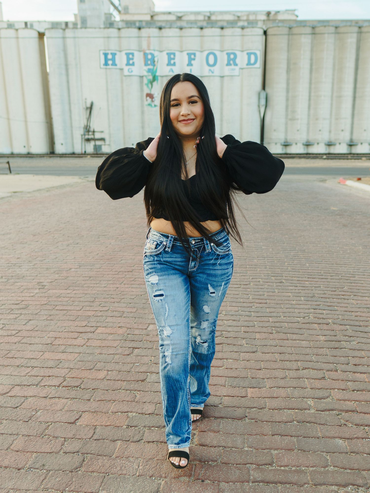Fashion portrait in front of grain silos featuring a crop top and distressed jeans outfit.