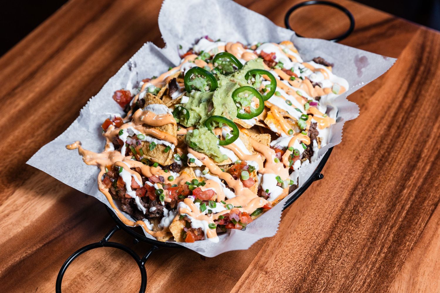 Close-up of nachos topped with jalapenos, cheese sauce and fresh garnishes.