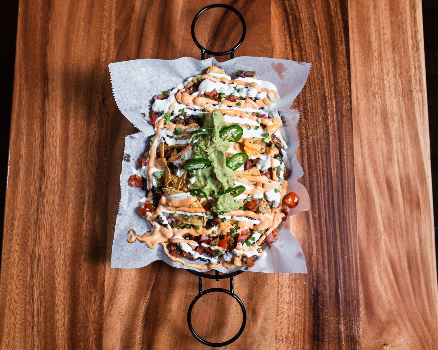 Loaded nachos topped with fresh jalapeños, melted cheese, spicy sauce and cilantro served on parchment paper.